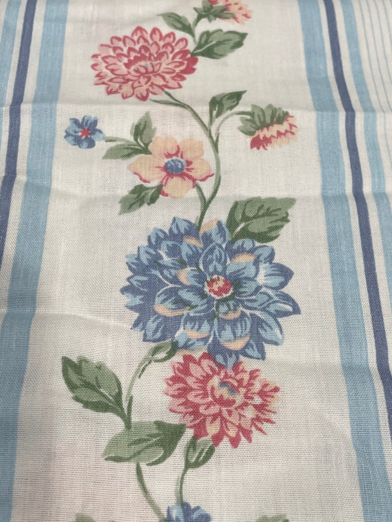 May include: A white fabric with blue stripes and a floral pattern. The flowers are pink, blue, and yellow. The fabric is perfect for crafting projects, quilting, or making clothing.