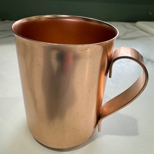 May include: A copper mug with a handle. The mug is shiny and has a smooth surface.