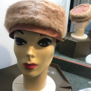 May include: A light brown fur hat with a pink satin band. The hat is on a mannequin head.