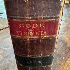 May include: A worn, brown leather-bound book with gold lettering that reads "CODE of VIRGINIA" and the year "1873" on the spine.