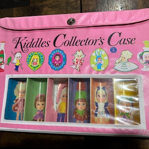 May include: Pink Kiddle Collector's Case with a flap closure. The case has a clear plastic window showing eight dolls in different outfits. The dolls are dressed in various colors and have different hairstyles. The case has a Kiddle Collector's Case title on the front.