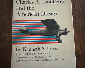 May include: Book cover with a red, white, and blue striped background. The book title is "The Hero" and the subtitle is "Charles A. Lindbergh and the American Dream". The cover also features a black and white image of an airplane.