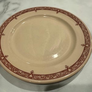 May include: A cream-colored ceramic plate with a brown floral design around the edge.