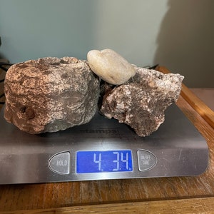 May include: Three rocks of different sizes and shapes on a digital scale. The scale reads 4.34 pounds.
