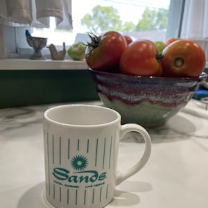 May include: White ceramic mug with blue and green stripes and the words "Sands Hotel Casino Las Vegas" printed on the front.