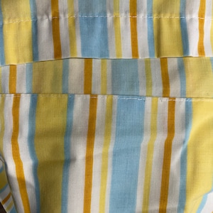 May include: Close-up of a striped fabric with yellow, blue, and white stripes. The fabric has a subtle texture and appears to be made of cotton.