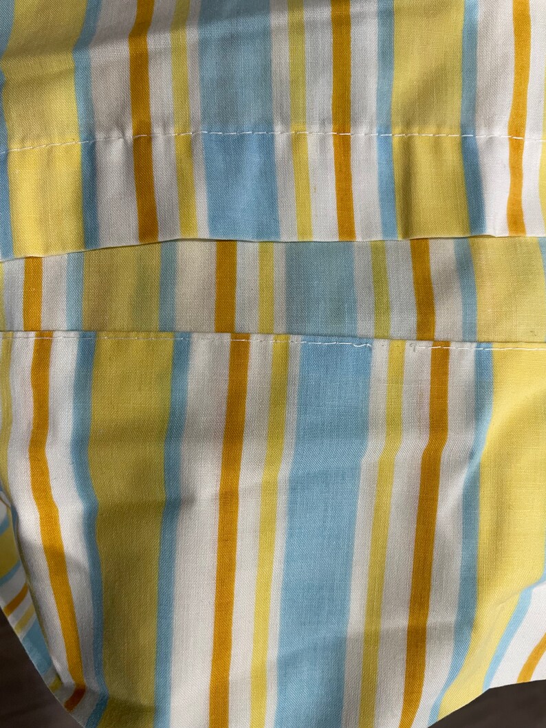 May include: Close-up of a striped fabric with yellow, blue, and white stripes. The fabric has a subtle texture and appears to be made of cotton.