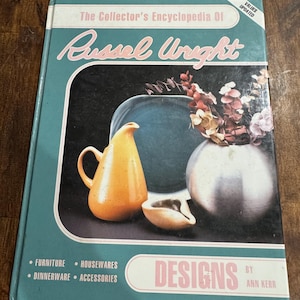 May include: A vintage book titled "The Collector's Encyclopedia Of Russel Wright" with a teal cover. The cover features a still life of orange and white pottery and a blue plate. The book's categories include furniture, dinnerware, housewares, and accessories.
