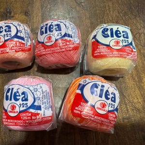 May include: Five spools of Cléa 125 mercerized cotton thread in various colors: peach, pink, coral, yellow, and orange. Each spool is wrapped in clear plastic with a label featuring the brand name, thread weight, and other details.