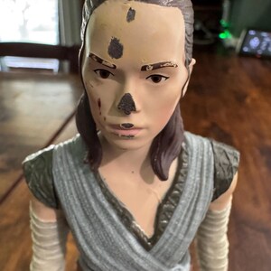 K&ouml;nnte beinhalten: Abgenutzte Actionfigur einer weiblichen Figur mit braunen Haaren in einem tiefen Pferdeschwanz. Die Figur tr&auml;gt ein grau-beiges Outfit mit Armwickeln. Das Gesicht weist dunkle Flecken und Farbabnutzung auf.