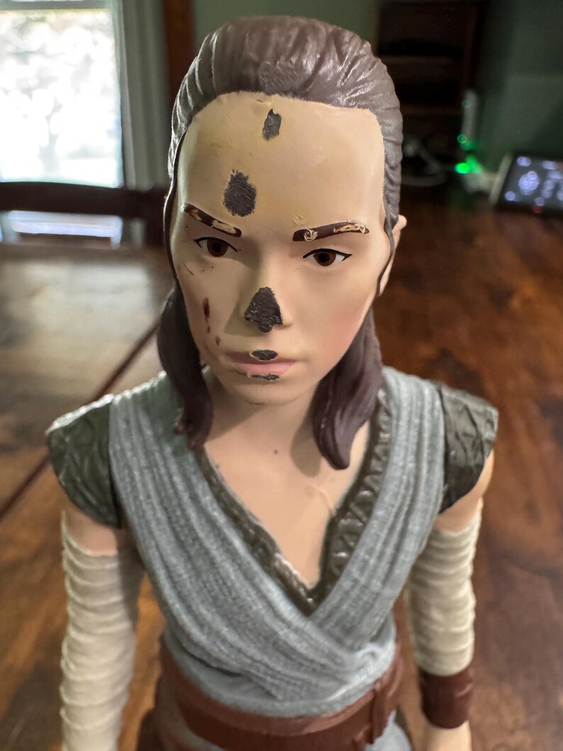K&ouml;nnte beinhalten: Abgenutzte Actionfigur einer weiblichen Figur mit braunen Haaren in einem tiefen Pferdeschwanz. Die Figur tr&auml;gt ein grau-beiges Outfit mit Armwickeln. Das Gesicht weist dunkle Flecken und Farbabnutzung auf.