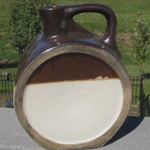 May include: A brown and white glazed ceramic pitcher with a handle. The pitcher has a wide mouth and a rounded body.