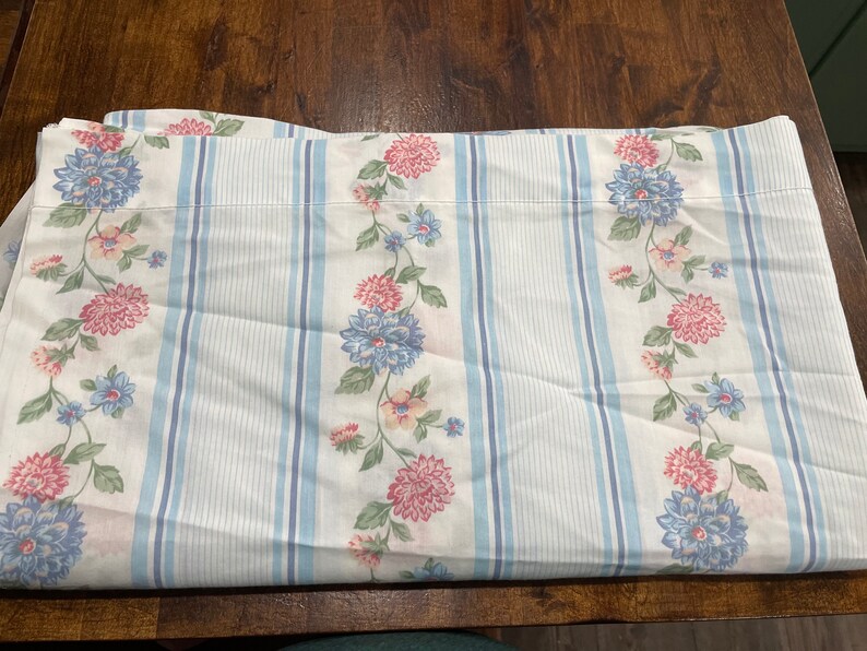 May include: White fabric with blue and pink floral pattern and blue and white stripes. The fabric is folded in half.