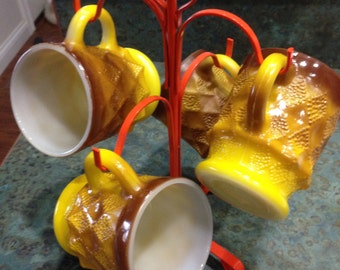 May include: Set of four vintage ceramic mugs with a geometric pattern in shades of brown and yellow. The mugs are hanging on a red metal mug rack.