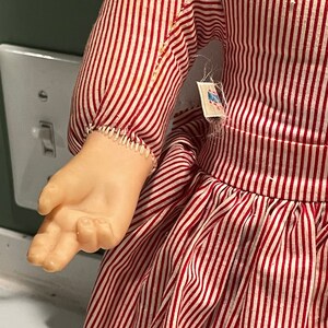 Puede incluir: Un vestido de rayas rojas y blancas con una etiqueta blanca que dice "Made in USA". El vestido tiene una falda fruncida y una manga larga.