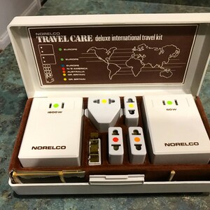 May include: A white travel adapter kit with the brand name "Norelco" and the text "Travel Care deluxe international travel kit". The kit includes two adapters, one with a 1800W rating and the other with a 90W rating. The kit also includes a variety of plug adapters for different countries.