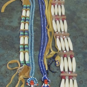 May include: Three beaded necklaces with bone beads and leather tassels. The necklaces are blue, white, and red. The necklaces are tied together with a brown leather cord.
