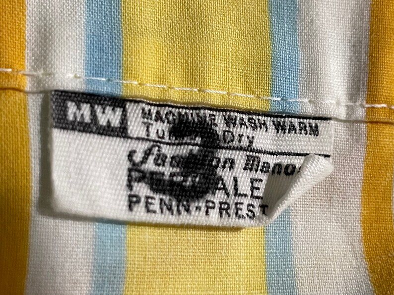 May include: White fabric with yellow and blue stripes. A white tag with black text reads "MW Machine Wash Warm Tumble Dry Fashion Manor Percale Penn-Prest".