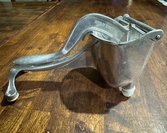 May include: A vintage, silver-toned citrus juicer with a lever arm and a bowl-shaped receptacle. The juicer has a sturdy design with a handle and is marked "MADE IN TAIWAN". It rests on three small feet.