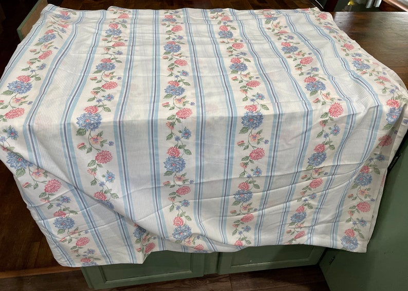 May include: White fabric with blue and pink floral stripes. The fabric has a soft, textured feel and is perfect for crafting projects or home decor.