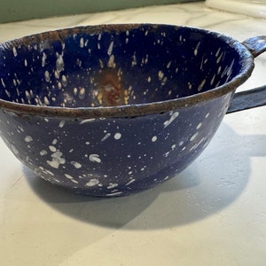 May include: A blue enamelware cup with white speckles and a metal handle. The cup has a rustic, vintage look.
