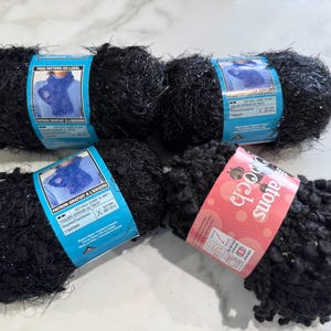 May include: Four skeins of black yarn with silver glitter. The yarn is packaged in clear plastic bags with colorful labels. The labels include the text "Free Pattern On Label" and "Boogie Doo-Dah".