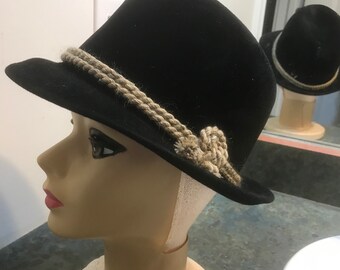 May include: A black felt fedora hat with a wide brim and a braided rope band. The band has a knot on the side.