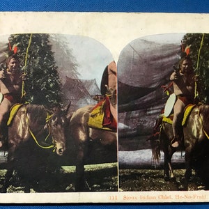 May include: A vintage stereoscopic card depicting a Sioux Indian Chief on horseback, wearing a feathered headdress and holding a bow and arrow. The image is in color and shows the Chief riding through a wooded area. The card is titled "Sioux Indian Chief. He-No-Fraud."
