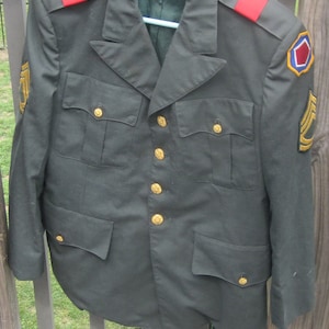 May include: A dark green military uniform jacket with gold buttons, red shoulder straps, and a patch on the right sleeve. The patch is blue, red, and white with a geometric design.