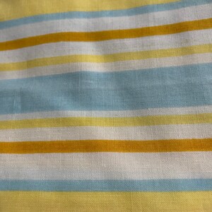 May include: A close-up of a striped fabric with alternating bands of yellow, light blue, and white.