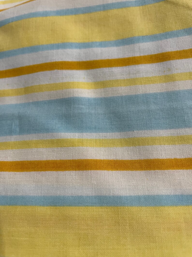 May include: A close-up of a striped fabric with alternating bands of yellow, light blue, and white.