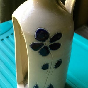 Puede incluir: Una jarra de cer&aacute;mica blanca con un dise&ntilde;o de flor azul. La jarra tiene un asa y un recorte en el lateral.