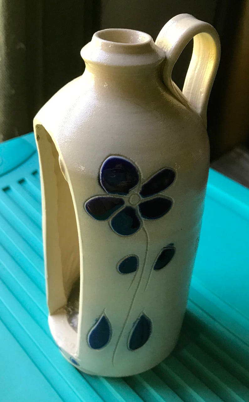 Puede incluir: Una jarra de cer&aacute;mica blanca con un dise&ntilde;o de flor azul. La jarra tiene un asa y un recorte en el lateral.
