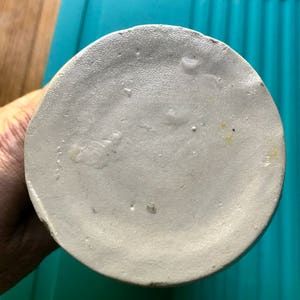 Puede incluir: La parte inferior de una jarra de cer&aacute;mica blanca con una superficie ligeramente texturizada. Hay algunas peque&ntilde;as manchas de color marr&oacute;n claro en la superficie.