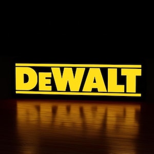 May include: The DeWalt logo is displayed in bright yellow block letters, outlined in black, against a dark background. The logo's reflection is visible on a wooden surface below. The word "DEWALT" is centered.