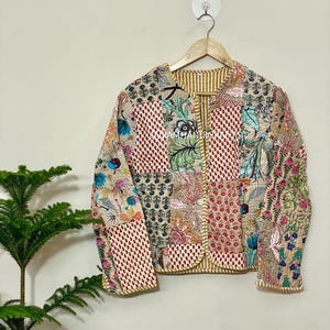 May include: A patchwork jacket with a variety of floral and geometric patterns in shades of beige, red, and blue. The jacket is quilted and has a striped lining. The sleeves and edges are trimmed with a gold-colored fabric.