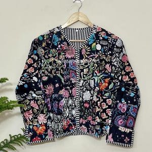 May include: Black floral print jacket with a striped V-neck and trim. The jacket features a variety of colorful flowers and foliage. The text "JAIRAMHANDICRAFTS" is visible on the jacket.