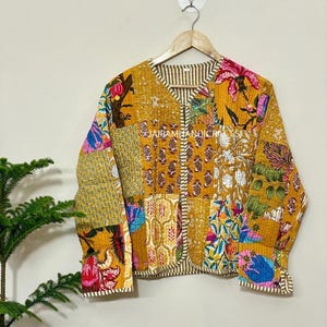 Könnte beinhalten: Senfgelbe Patchwork-Jacke mit floralen und geometrischen Mustern in Rosa und Blau. Die Jacke hat einen V-Ausschnitt und lange Ärmel. Der Text "JAIRAMHANDICRAFT" ist auf der Jacke zu sehen.