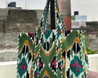May include: A large, quilted tote bag with a vibrant, geometric pattern in shades of green, black, white, pink, and gold. The bag has sturdy handles and a structured shape, suitable for carrying various items.