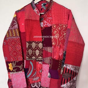 May include: A patchwork jacket in shades of red, burgundy, and pink, with a mandarin collar. The jacket features a variety of fabric patterns and textures, including floral and geometric designs. The text "JAIRAMHANDICRAFTS" is visible on the jacket.