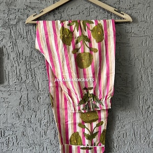 Puede incluir: Pantalones de pijama a rayas rosas y blancas con dise&ntilde;os florales verdes colgados de una percha de madera. Los pantalones tienen cintura con cord&oacute;n y est&aacute;n hechos de tela ligera. El texto "Jairamhandicrafts" es visible.