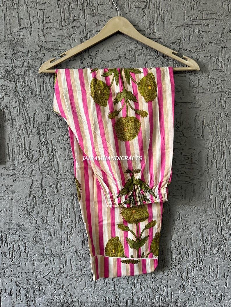 Puede incluir: Pantalones de pijama a rayas rosas y blancas con dise&ntilde;os florales verdes colgados de una percha de madera. Los pantalones tienen cintura con cord&oacute;n y est&aacute;n hechos de tela ligera. El texto "Jairamhandicrafts" es visible.