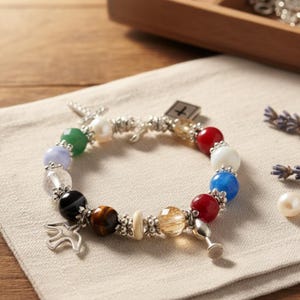 May include: A colourful beaded bracelet with various gemstones and silver-toned details. The bracelet includes red, white, blue, green, and other coloured beads. Charms include a cross, a dove, and a small chalice.