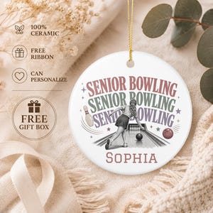 May include: A round white ceramic ornament featuring a graphic of a person bowling on a lane. The text reads SENIOR BOWLING in stacked, multi-colored lettering, with the name SOPHIA printed at the bottom. The ornament includes a gold hanging string.