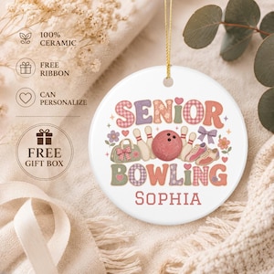 May include: A round white ceramic ornament featuring the text SENIOR BOWLING and the name SOPHIA. The graphic includes a red bowling ball, white pins, a green bowling bag, and bowling shoes, decorated with small flowers, hearts, and a bow.