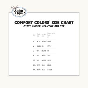 May include: A size chart for Comfort Colors C1717 unisex heavyweight tees. The chart includes measurements for width, length, and sleeve center back in inches for sizes S through 4XL. The Saint Flora logo is in the upper left corner.