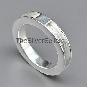 Puede incluir: Un anillo de plata con la parte superior plana y los lados texturizados. El anillo tiene un diseño simple y moderno y está sobre un fondo gris. El texto "The Silver Sellers" es visible en el anillo.