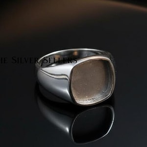 Op de afbeelding: Een gepolijste zilveren ring met een vierkante zetting. De ring wordt gepresenteerd op een reflecterend zwart oppervlak. De tekst "THE SILVER SELLERS" is zichtbaar op de ring.