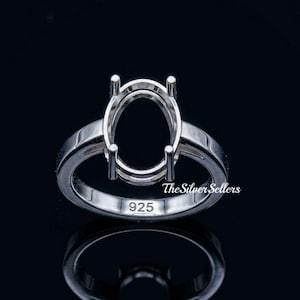 Könnte beinhalten: Ein Silberring mit ovaler Fassung, bereit für einen Edelstein. Der Ring hat ein geteiltes Schaftdesign und ist mit "925" gestempelt. Der Ring wird auf einer reflektierenden schwarzen Oberfläche präsentiert.