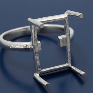 Op de afbeelding: Een zilveren ringzetting met een rechthoekige bovenkant, ontworpen om een edelsteen te bevatten. De ring heeft een gepolijste band en een gedetailleerde zetting, perfect voor het maken van sieraden. De tekst "The Silver Sellers" is zichtbaar.